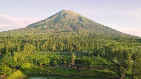 Aerial-flyover-ARTIFICIAL-LAKE-for-collecting-rainwater-during-dry-season-for-agriculture---Mountain-Sindoro-in-background,Asia