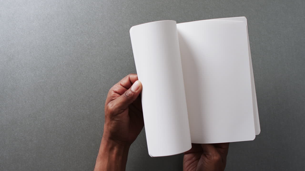 Close up of hand leafing through book with copy space on gray background in slow motion