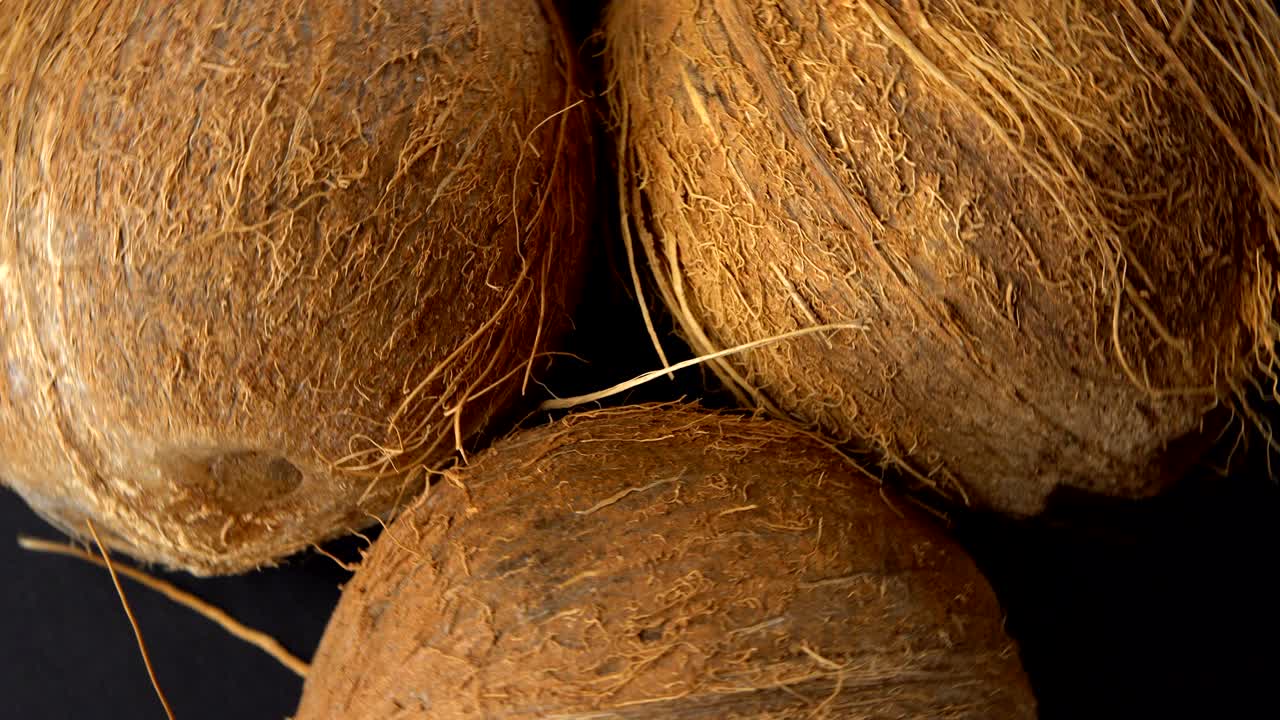 tres cocos tropicales maduros girando sobre un fondo negro. frutas tropicales y concepto de alimentos. bucle