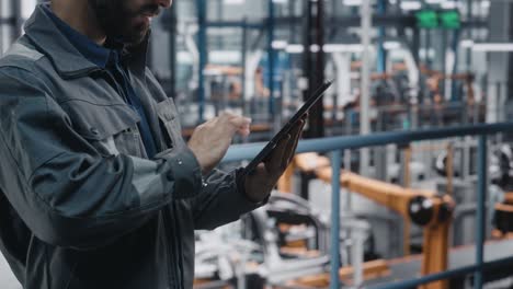 portrait of automotive industry engineer in safety glasses and uniform using tablet at car factory facility. professional assembly plant specialist working on manufacturing modern electric vehicles.