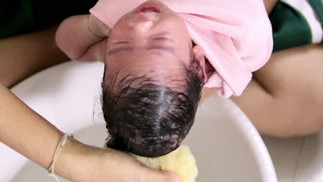 un bebé recién nacido dando un baño usando una esponja amarilla suave y agua limpia para enjuagar algunos residuos jabonosos de su cabeza peluda