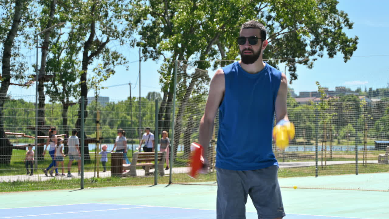 Close up of a man in a blue shirt playing pickleball with a red racket on a sunny day