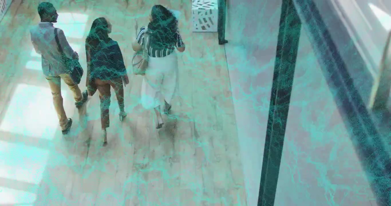 Three colleagues entering office corridor and walking under light patches conversing near column