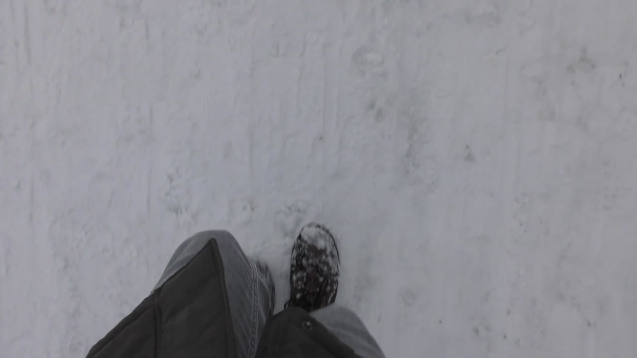 The Person's Legs Are Walking Along A Snowy Road During Cold Winter Day