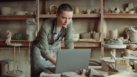 female potter using laptop in workshop