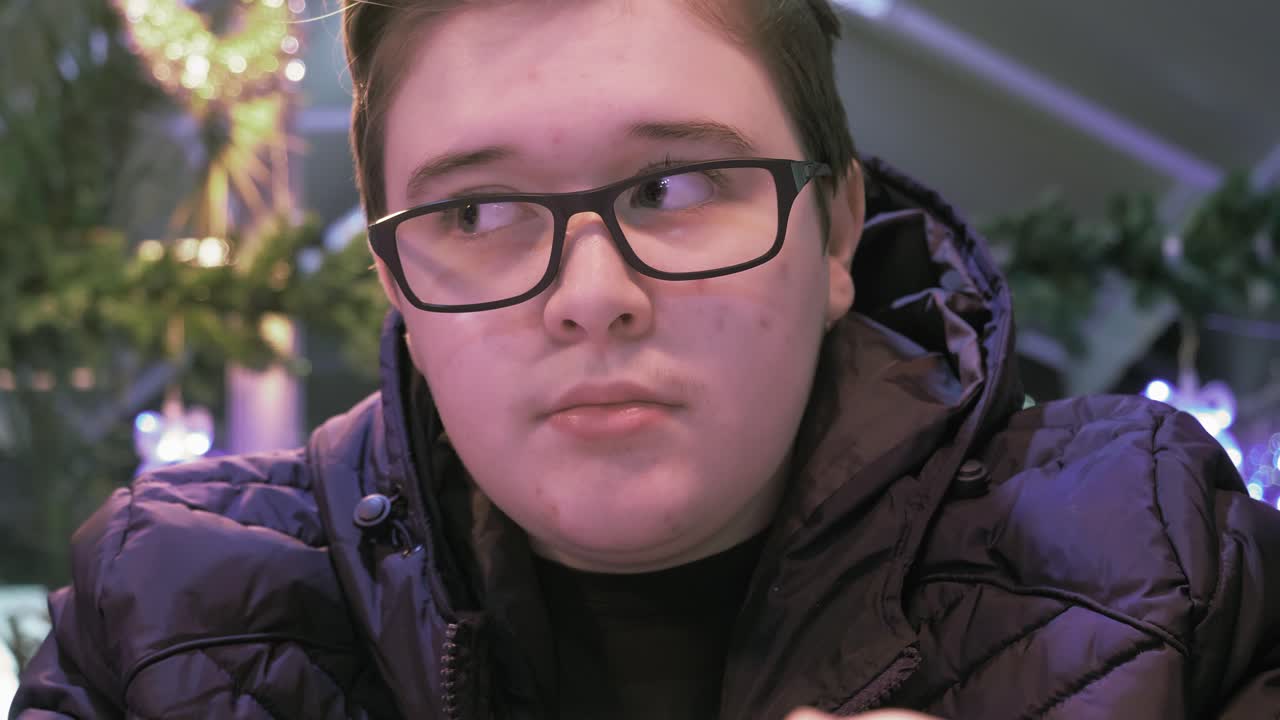 Adolescente sentado en un café, moviendo la cabeza al ritmo de la música, mientras la luz de su teléfono parpadea en su cara.