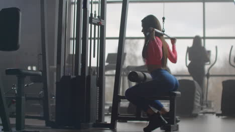 a young girl with pumped buttocks and a slim body does an exercise on the back muscles on a special training machine. she uses extra load for better results.