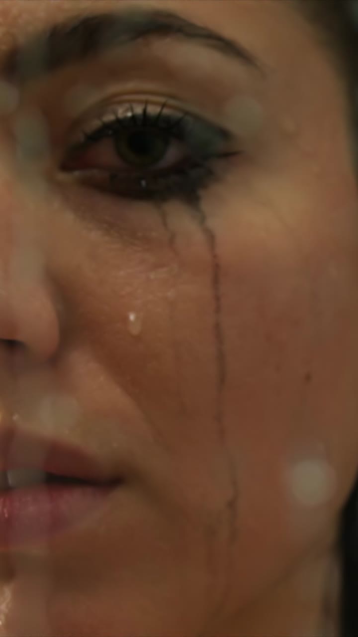 Young woman with wet face and ruined mascara crying behind glass in shower closeup sequence