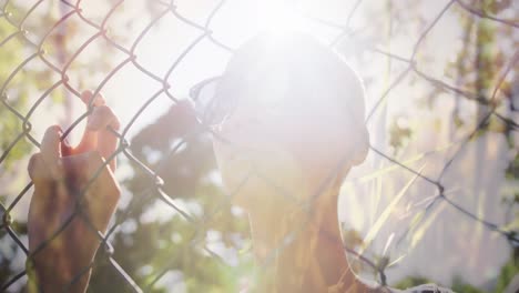 animación de hierba y senderos de luz sobre mujer biracial con gafas de sol, de pie detrás de la valla.