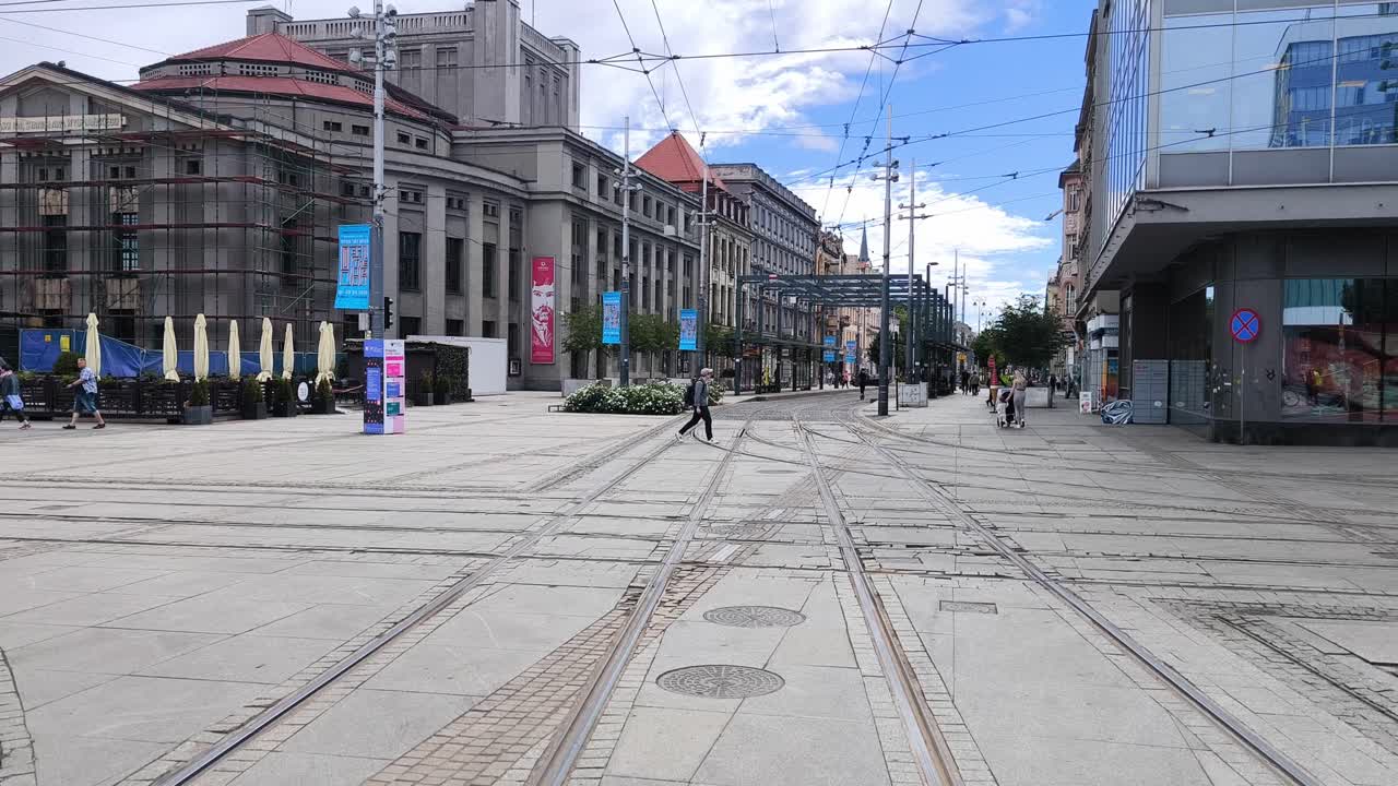 City street with multiple tram tracks and historic buildings, featuring pedestrians and an outdoor cafe area