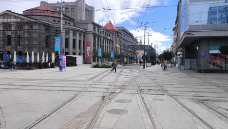 city street with multiple tram tracks and historic buildings, featuring pedestrians and an outdoor cafe area