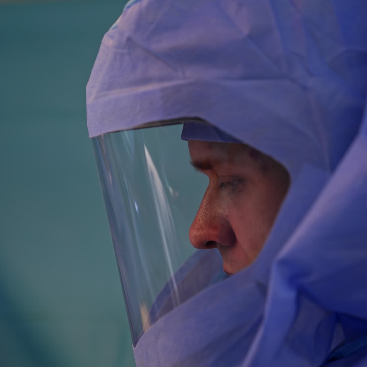 Medico in tuta protettiva concentrato sull'operazione. Ritratto di un chirurgo che esegue un intervento. Primo piano laterale
