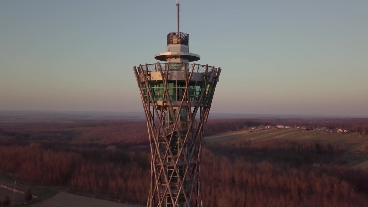 Sakin bir kırsal ortamda, çıplak ağaçlar ve altın ışıkla çevrili çarpıcı bir kafes gözlem kulesinin etrafında süzülen dramatik drone videosu.