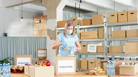 caucasian woman volunteer in facial mask packing donation boxes in charity warehouse