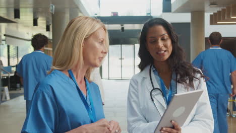 female medical staff in white coats and scrubs use digital tablet in informal meeting in hospital