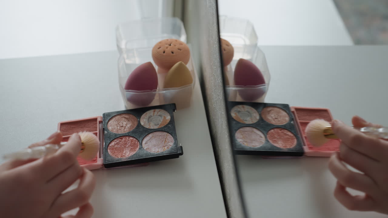 Closeup of beauty routine with reflections. Intimate morning makeup session shown with reflection and tools. Detailed view of woman applying eye makeup using sponges in soft morning light