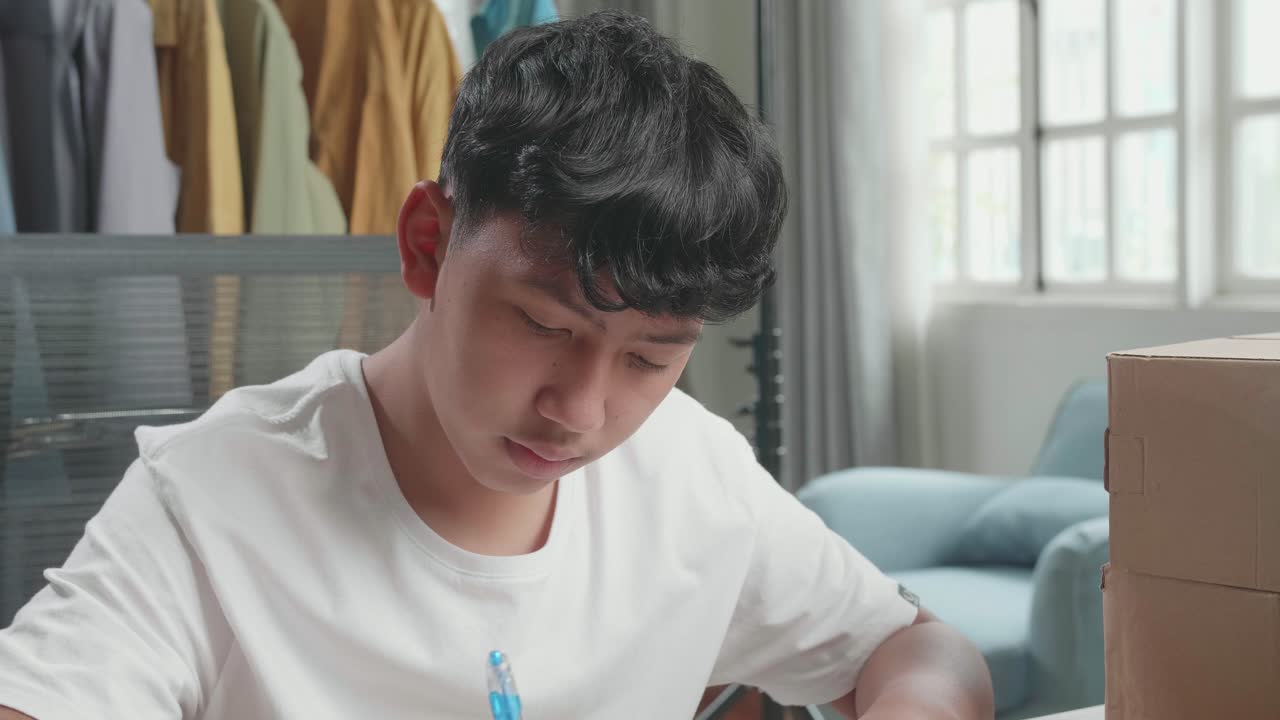 Close Up Of Asian Man Online Seller With Package Writing In The Notebook While Selling Clothes At Home