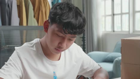 close up of asian man online seller with package writing in the notebook while selling clothes at home