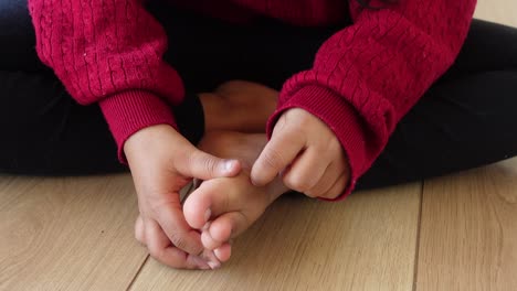 a young girl sitting on a wooden floor with her feet up, touching her toes.