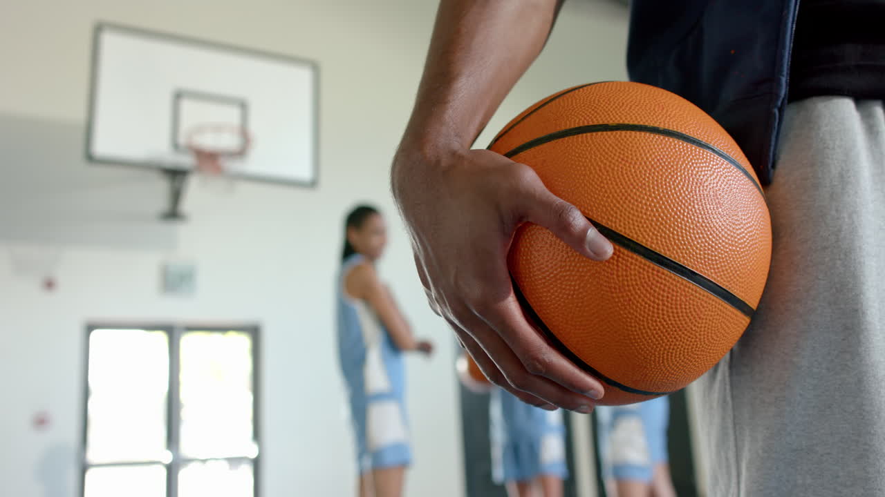 Holding basketball, player standing in gym with teammates in background