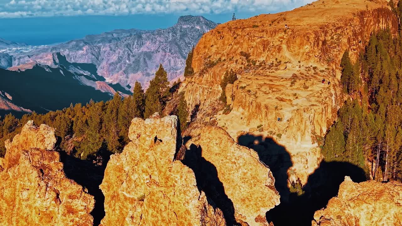 Pemandangan matahari terbenam pegunungan Gran Canaria dengan formasi batuan dan pepohonan.