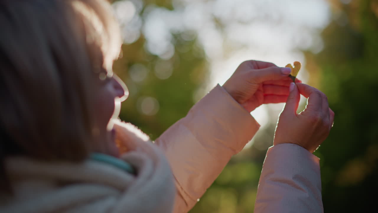 close up of woman holding heart shaped flower cutout toward sunlight with warm smile, golden light shining through shape onto face, soft bokeh foliage