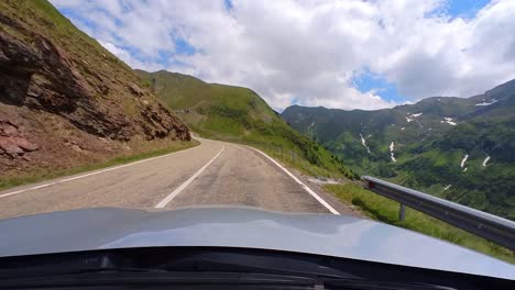 transfagarasan road from a car, surrounded by lush vegetation, tall mountains, clear blue sky with fluffy white clouds, snow on the side of the road summer vacation, romania