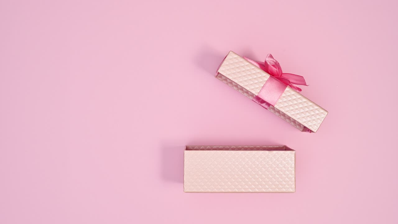 Regalo rosa pastello con nastro rosa che appare e si apre su sfondo rosa pastello. Stop motion.