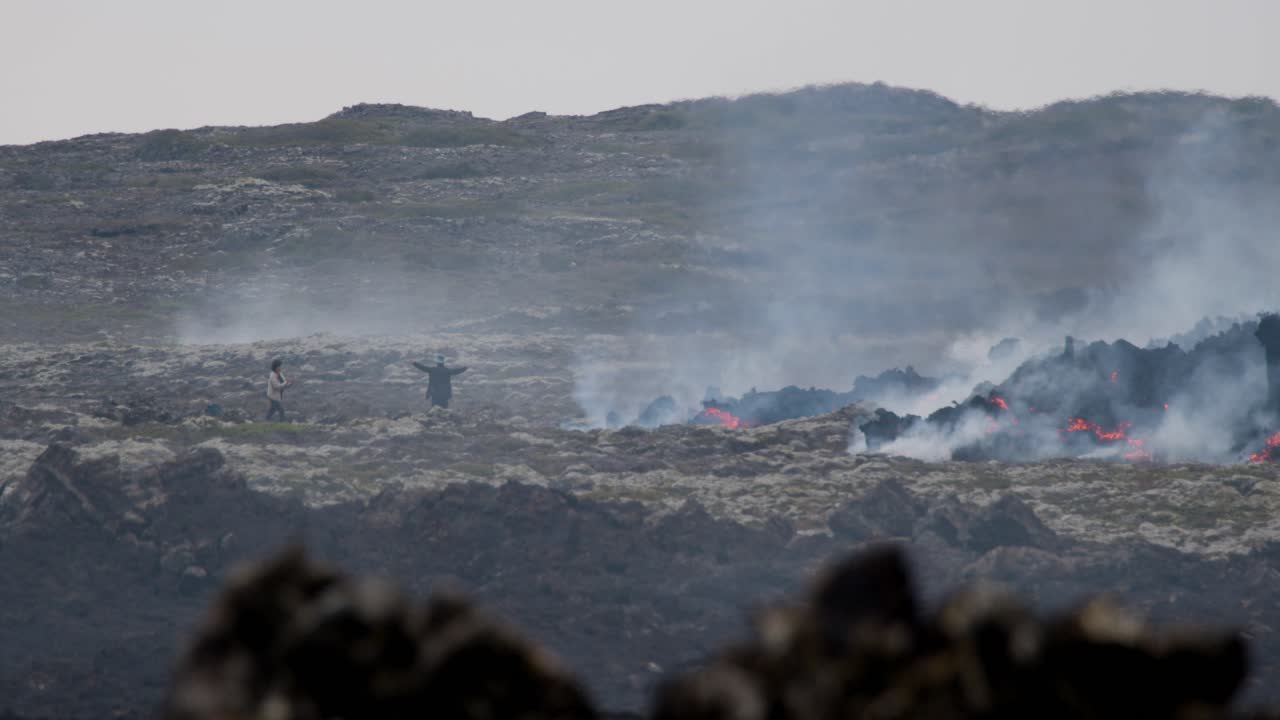 Person taking a picture of someone posing near molten lava flowing from Grindavik volcano, Sundhnúkur crater, Iceland.