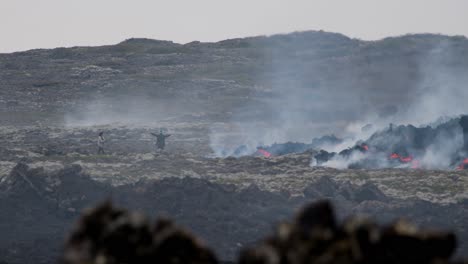 person taking a picture of someone posing near molten lava flowing from grindavik volcano, sundhnúkur crater, iceland.