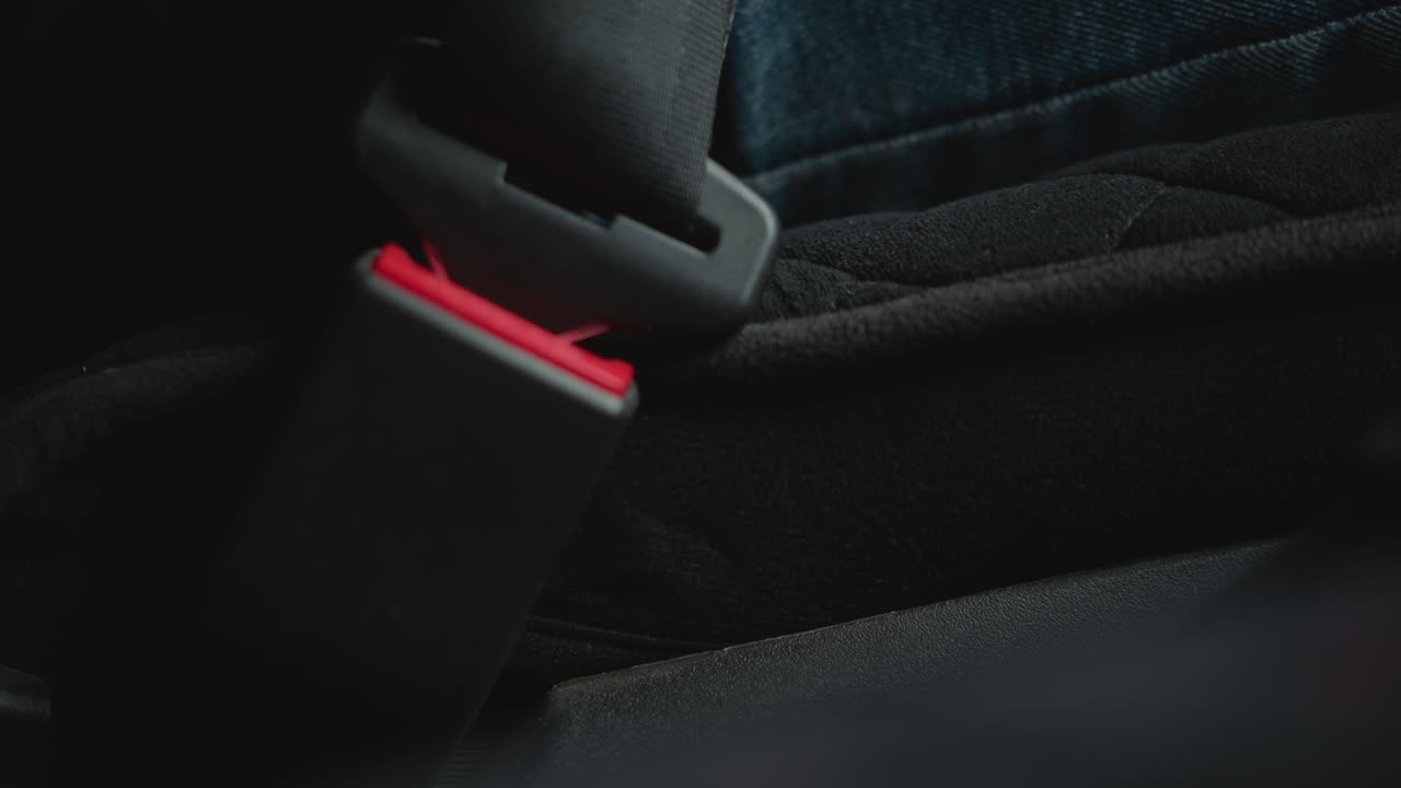 Close up of automobile enthusiast hand locking seat belt buckle in car cabin focusing on finger pressing red latch safety ritual ambient lighting textured trim during winter commute