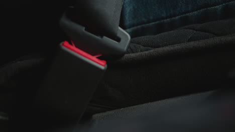 close up of automobile enthusiast hand locking seat belt buckle in car cabin focusing on finger pressing red latch safety ritual ambient lighting textured trim during winter commute