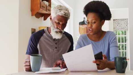 african american couple drinking coffee and paying bills in kitchen