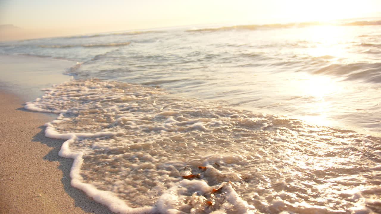 부드러운 파도가 해가 지는 모래 해변을 고, 지평선에 따뜻한 빛이 빛나고, 복사 공간이 있습니다.
