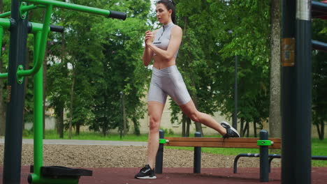 una mujer joven en un parque realiza sentadillas en una pierna en un banco en ropa deportiva en el verano. atletismo mujer caucásica entrena en el parque