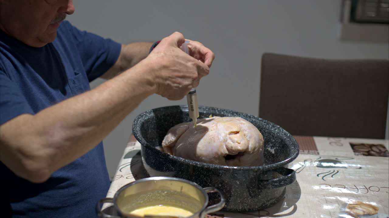 Close up of an hispanic latin mature man with mustache injecting a raw turkey in a cooking pot preparing for christmas thanksgiving