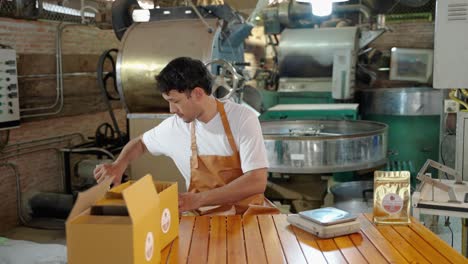 young man who owns a small coffee roaster and a young start-up is packing the finished coffee beans into bags and boxes.