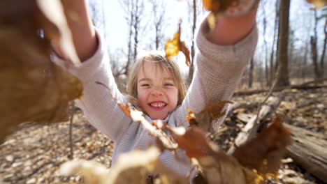 happy little girl tossing leaves into the air in an autumn forest