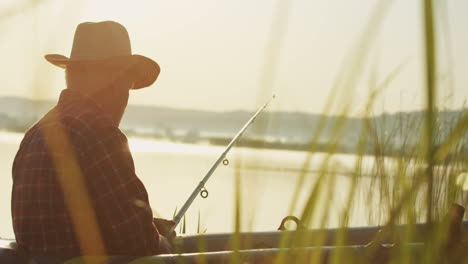 side view of a senior caucasian man in a hat catching a fish in a boat at the lake in the morning