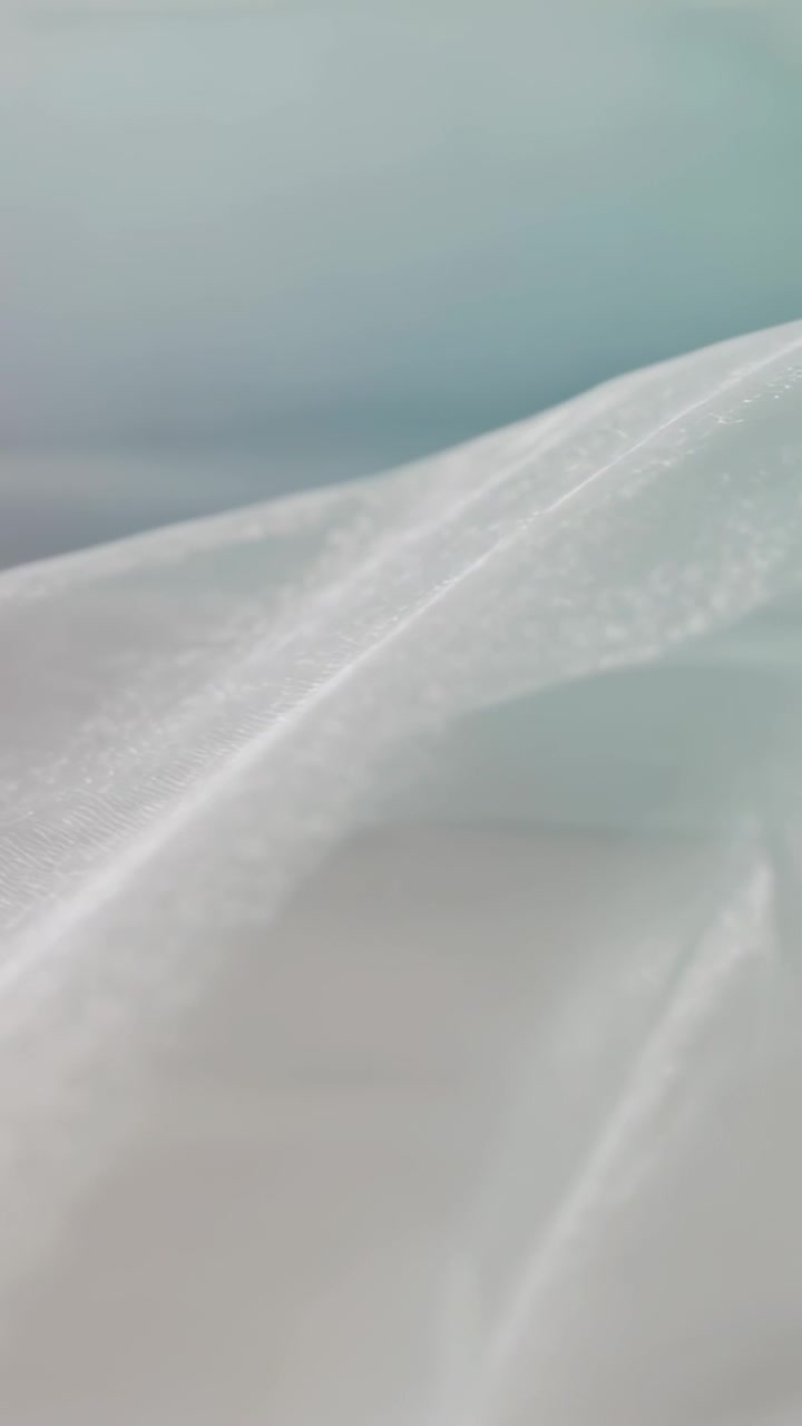 Vídeo vertical: Tecido branco transparente subindo suavemente, formando uma crista angular sobre um fundo azul-esverdeado suave