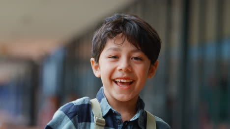 portrait of smiling male elementary school pupil outdoors with backpack at school