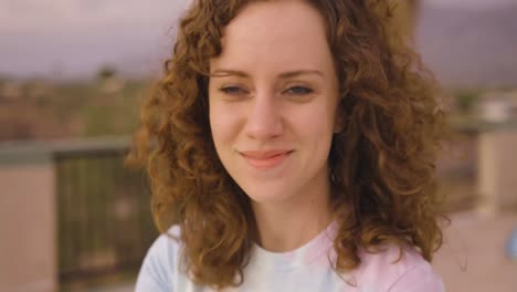 lovely young woman looks at camera and laughs while wind blows her curly red hair