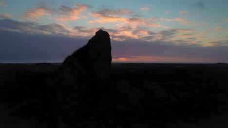 silhouette of a giant rock at whatipu beach at sunset in new zealand