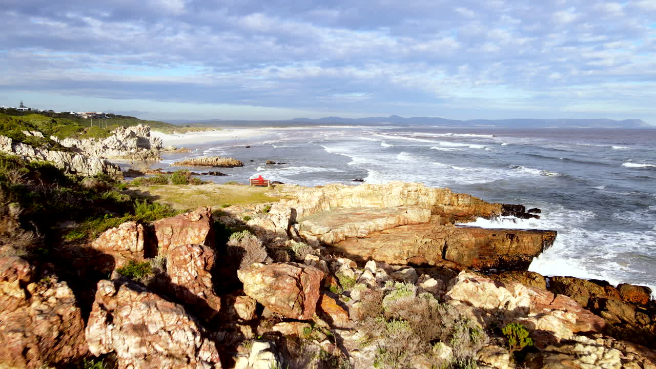 한 남자가 바위가 있는 헤르마누스 해안가의 벤치에 앉아 풍경이 아름다운 그로토 해변을 바라보고 있다.