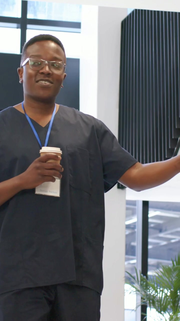 Vertikal video: Gående mand i hospitalsuniform går ind i lobbyen, døre åbner, hilser på kollega med kop og ID.