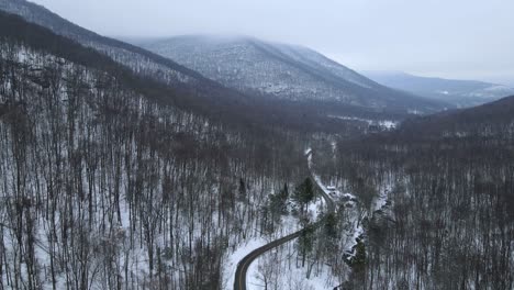 Abstieg-In-Ein-Schneebedecktes,-Bewaldetes-Bergtal-Im-Winter-Mit-Bergen-Und-Einer-Abgelegenen-Straße-Und-Wolkenhimmel