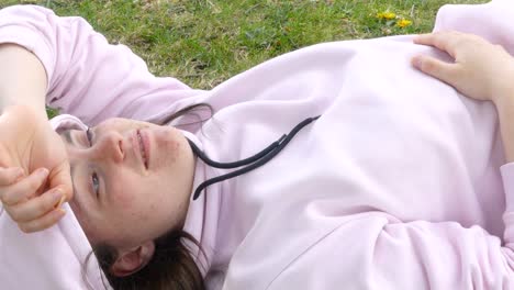 Young,-happy-and-calm-teenager-girl-with-a-pink-hoodie-lying-down-on-the-grass