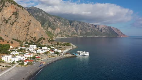 Embark on a journey with the drone as it flies near the stunning coast of Crete island, capturing a cruise ship near the city and the majestic mountains in the background.