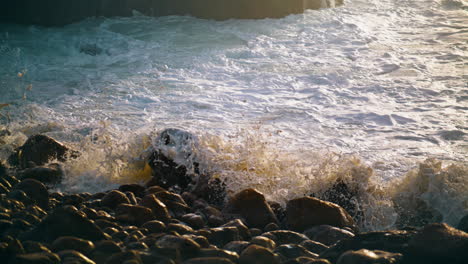 Olas-Golpeando-Las-Rocas-De-La-Playa-A-La-Luz-Del-Sol-De-La-Mañana.-Primer-Plano-De-Salpicaduras-De-Agua-Espumosa