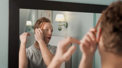 Portrait-of-a-curly-handsome-man-combing-his-hair-with-a-wooden-comb